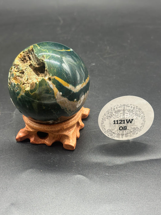 Ocean Jasper Sphere (1121W08) on a wooden stand, featuring green and white marbled patterns, with a circular sticker displaying numbers and letters nearby.