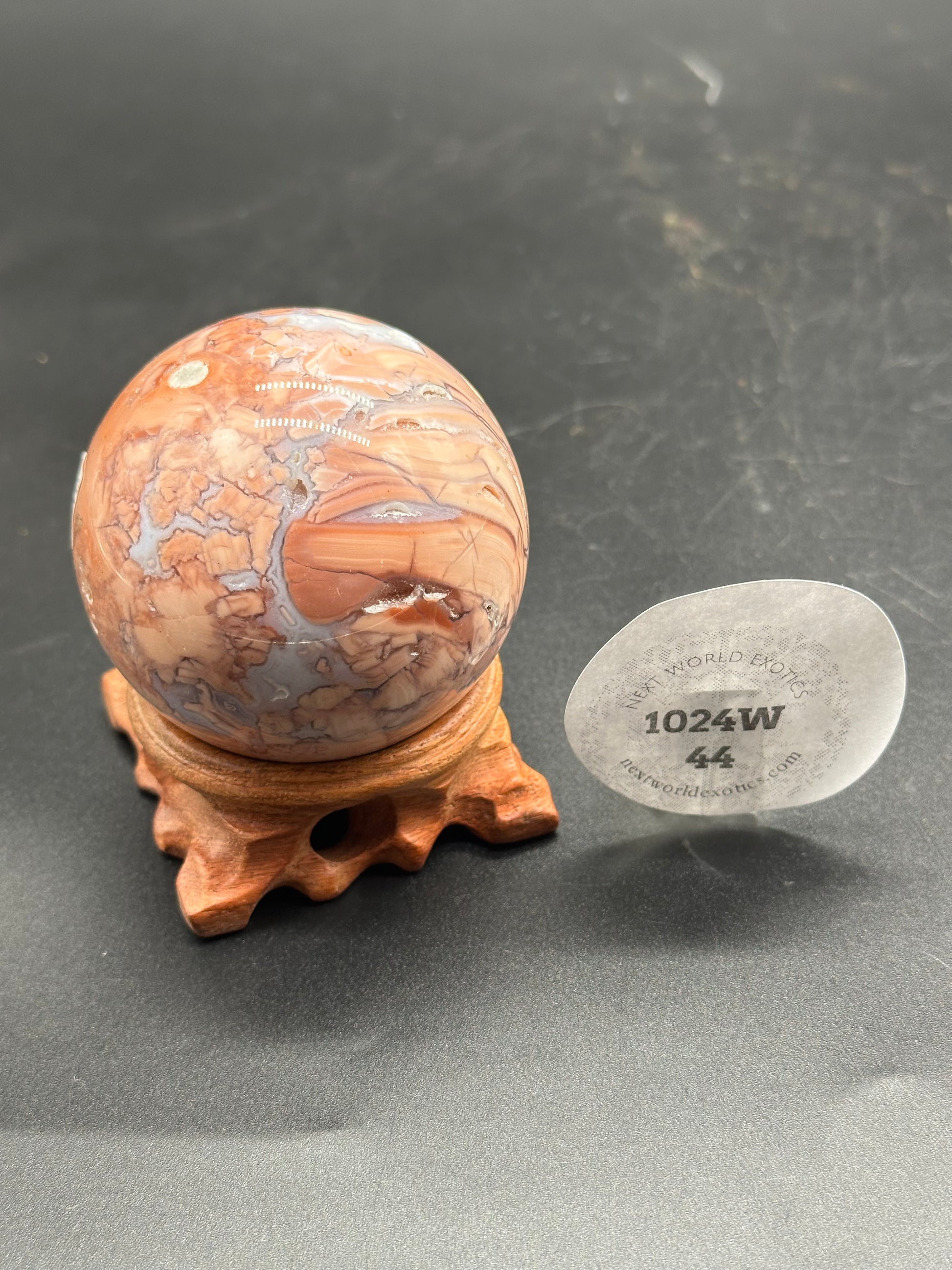 Pink Agate Sphere (1024W44) displayed on a wooden stand, showcasing its marbled pattern and round shape, emphasizing its natural mineral beauty.