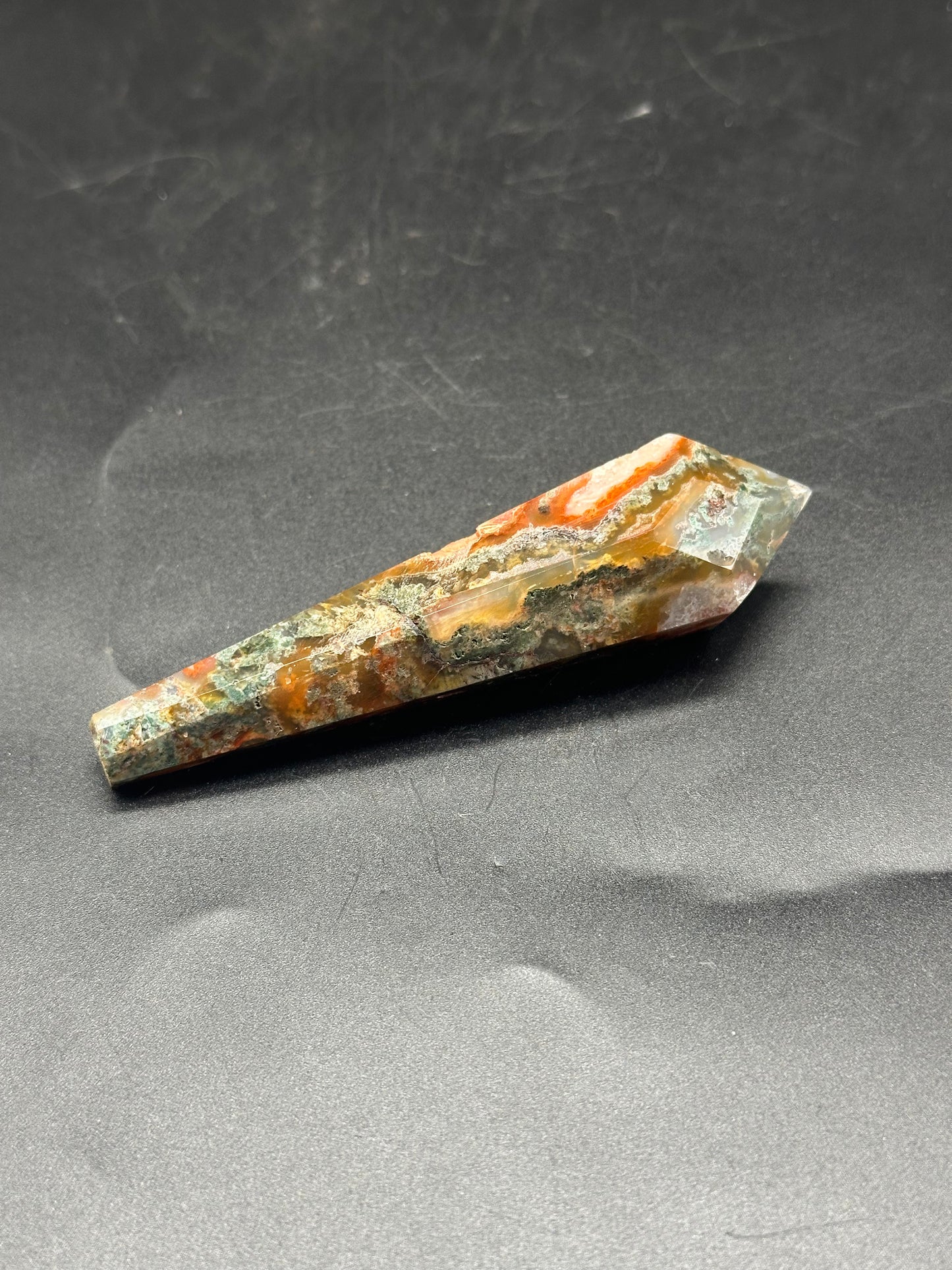 Red Moss Agate Scepter (103W48) featuring a crystal point on a black surface, highlighting its intricate details and natural mineral formation.