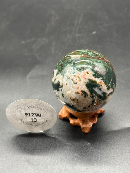 Red Moss Agate Sphere (912W13) displayed on a stand next to a round disc with text, highlighting its use in home decor and personal collections.