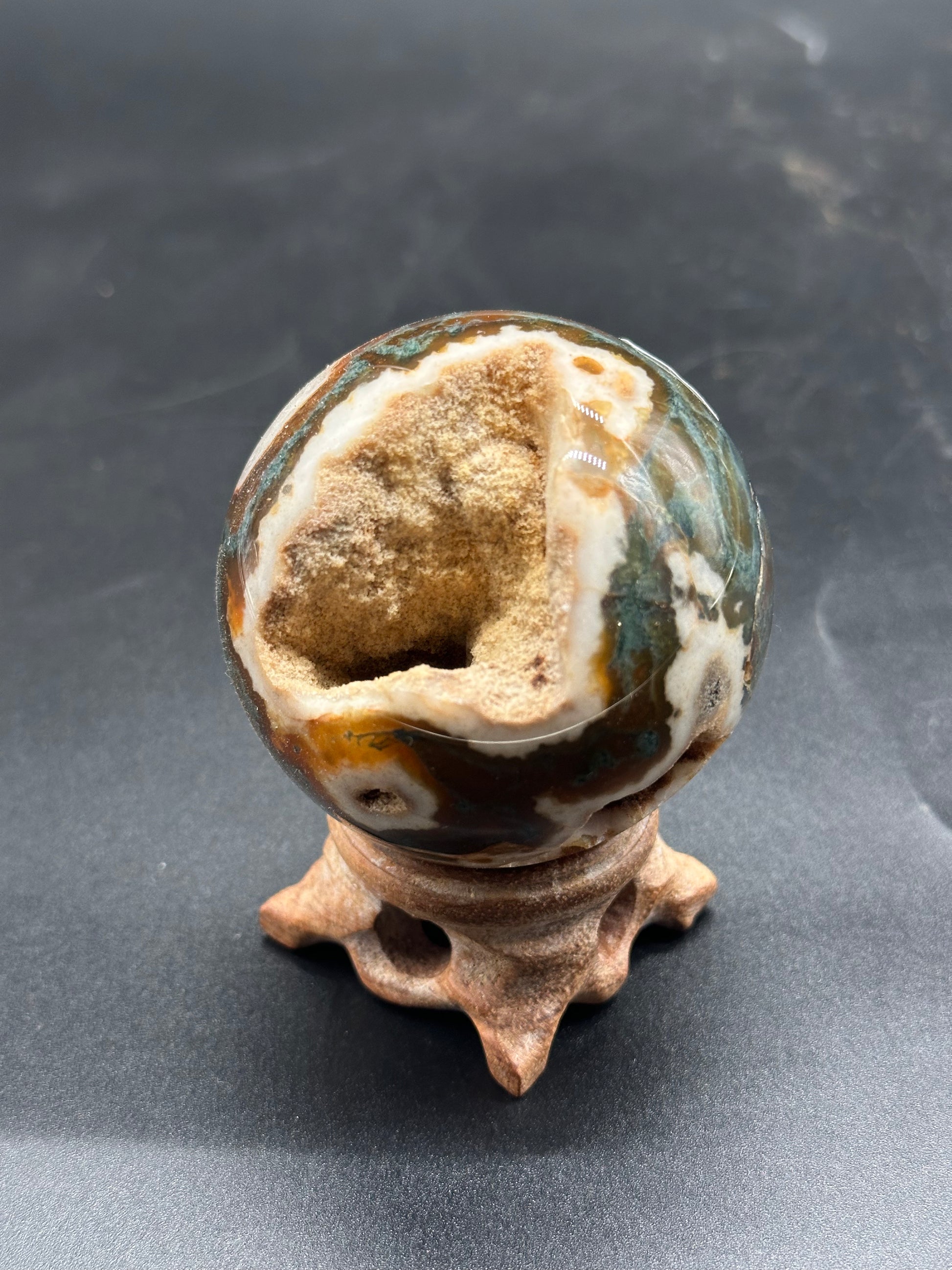 Red Moss Agate Sphere (1024W45) displayed on a stand, featuring a distinct hole and textured stone surface, ideal for crystal enthusiasts and collectors.