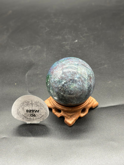 Ruby Kyanite Sphere (829W06) on a wooden stand, showcasing the polished, round surface of the mineral.