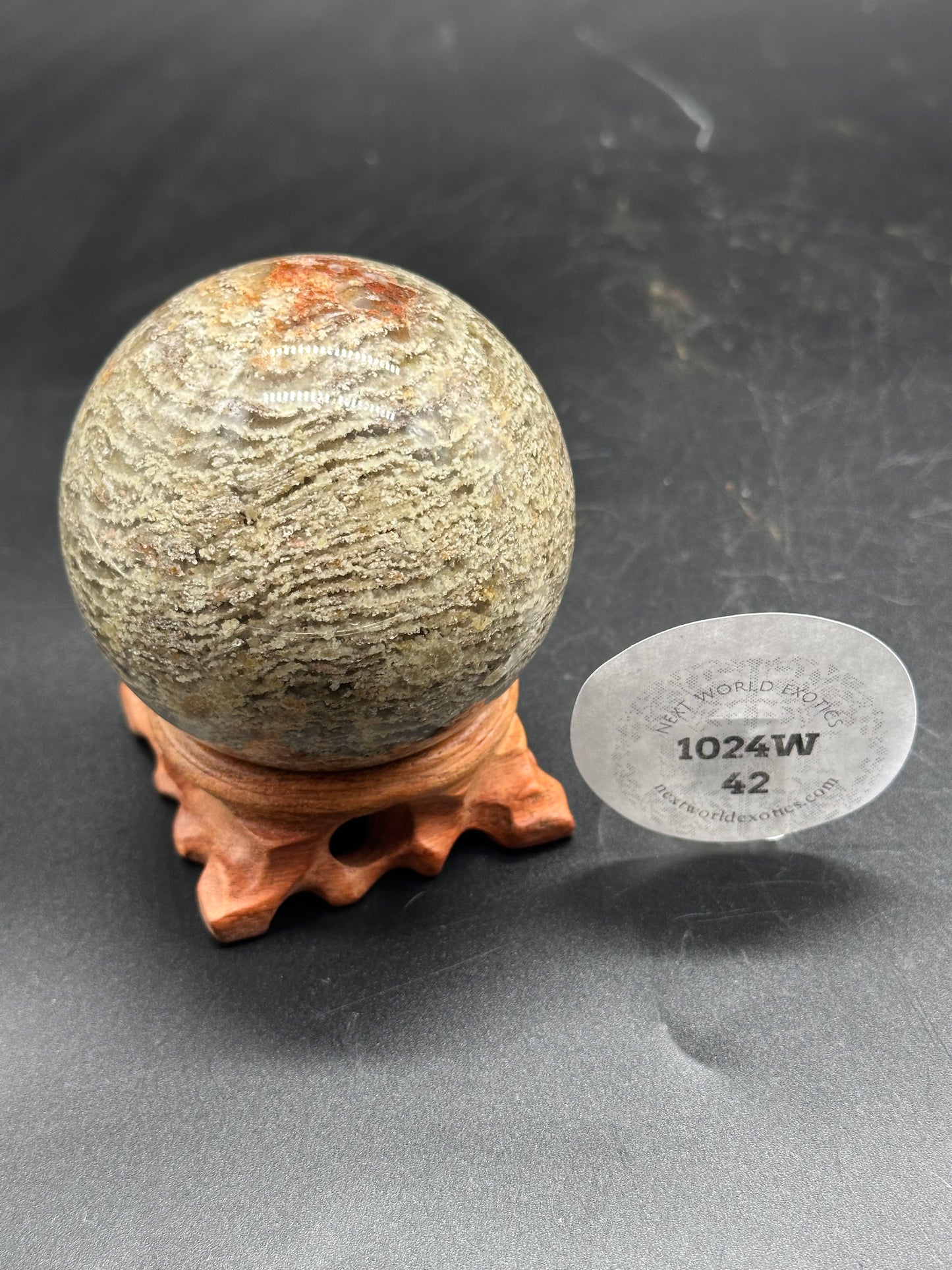 Thousand Layer Quartz Sphere (1024W42) displayed on a wooden stand, with a close-up of a transparent sticker featuring black text.