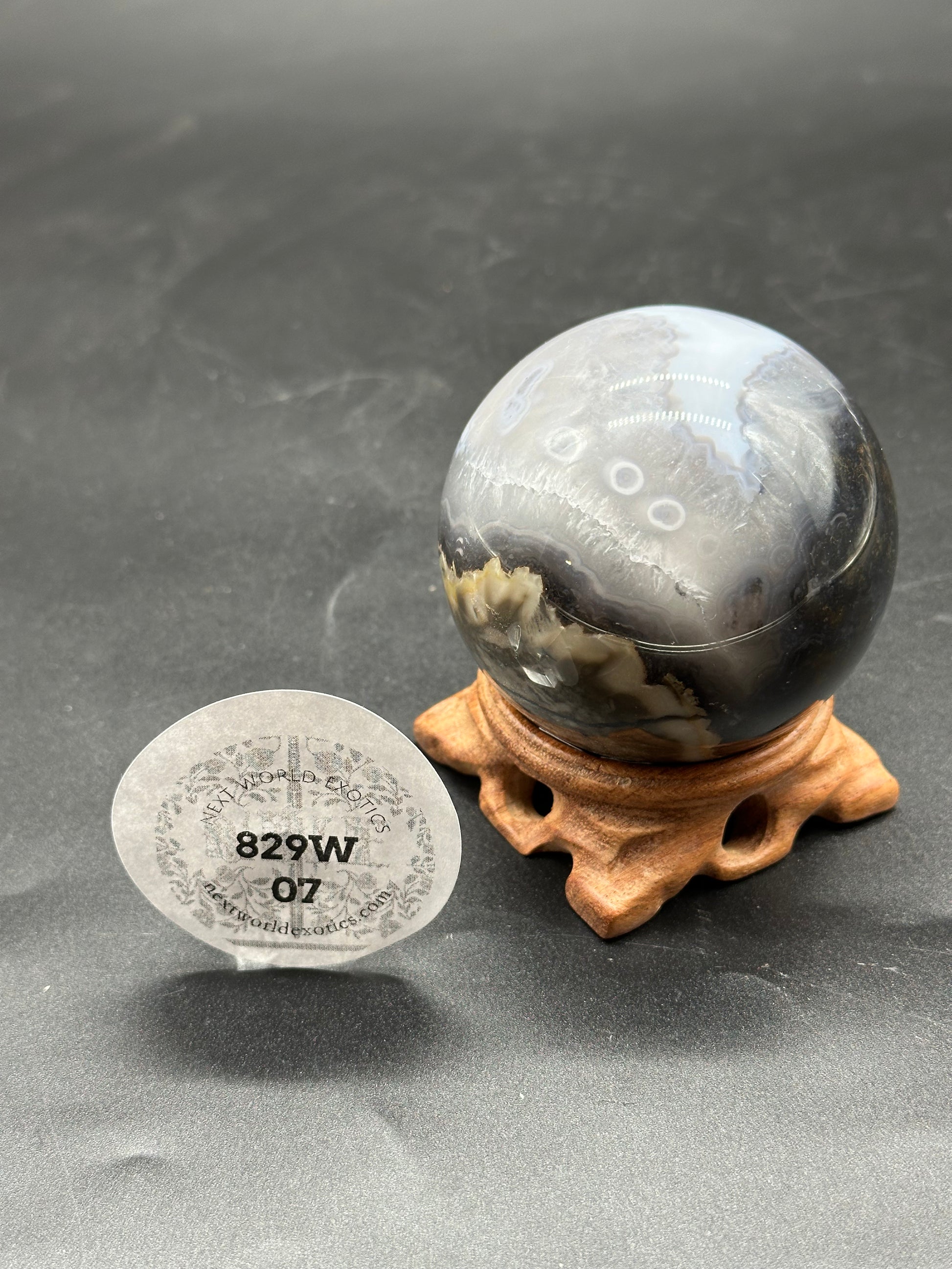 Volcanic Agate Sphere (829W07) displayed on a wooden stand, highlighting its smooth, rounded surface.