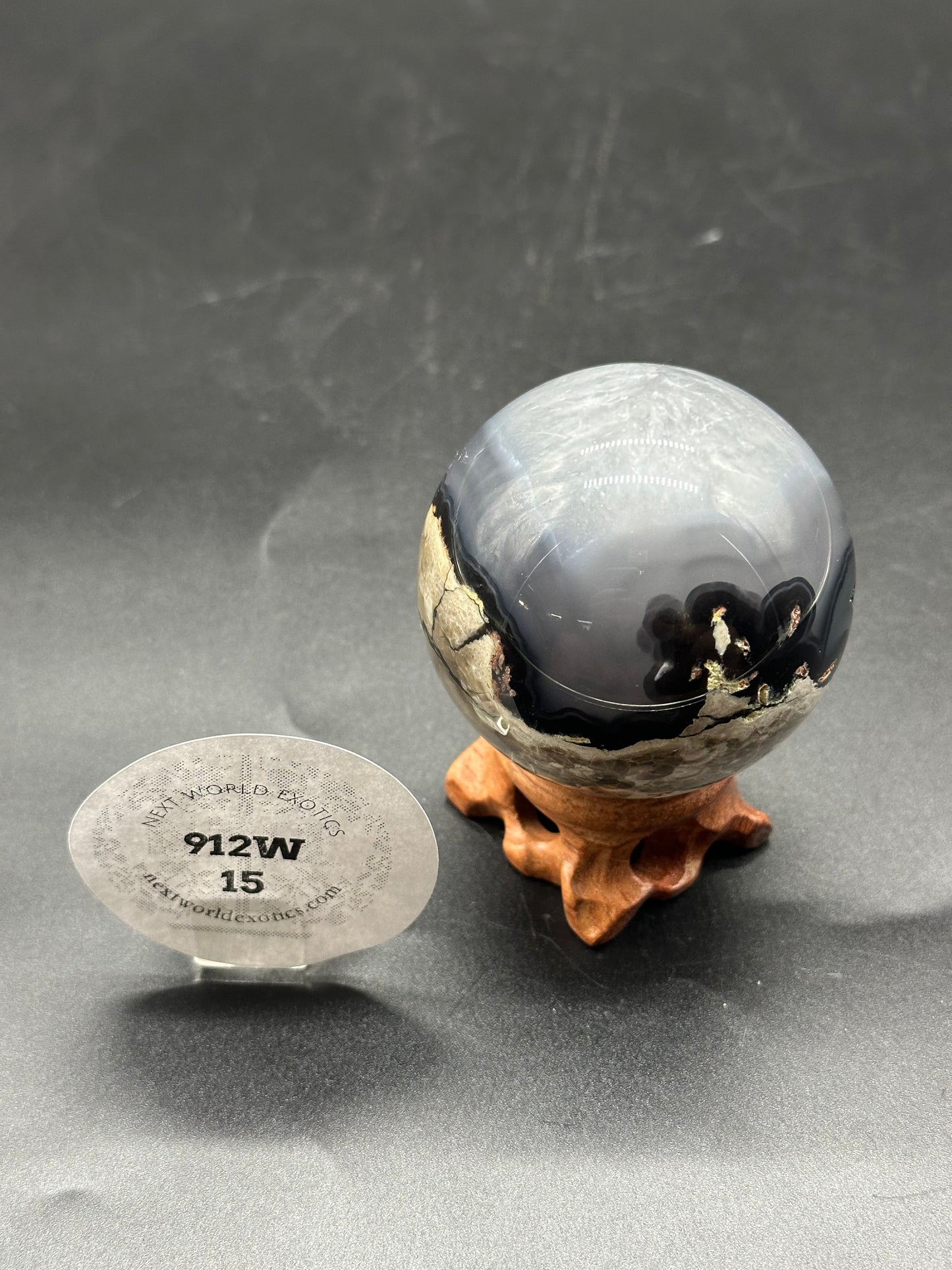 Volcanic Agate Sphere (912W15) displayed on a wooden stand. The glass sphere reflects nearby objects, highlighting its intricate patterns and polished surface.