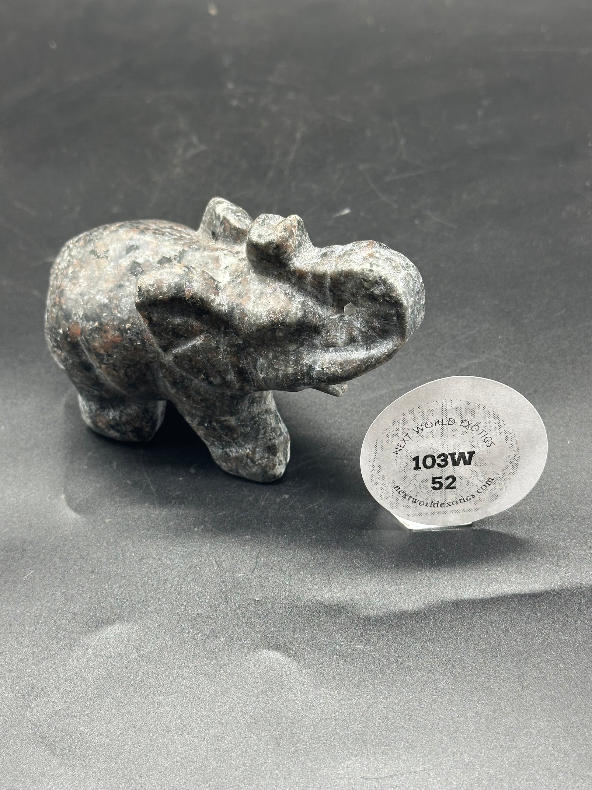 Yooperlite Elephant Carving (103W52) - a small stone elephant statue displayed on a black surface, featuring intricate carving details.